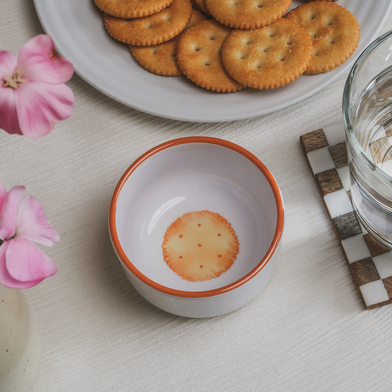 Looking down on the crackers Macro Bowl, showing a colorful illustration of a golden round cracker on the bottom of the bowl, with flowers, more crackers, and a glass of water in view around it.