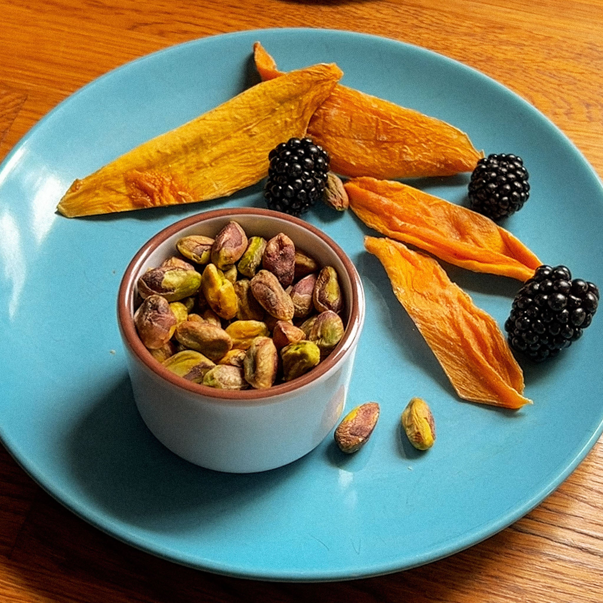 Pistachios, dried mango, and a couple blackberries nicely placed on a blue plate.